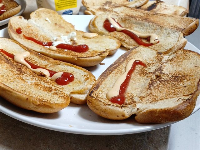 A plate of toasted buns dressed with ketchup and sauce during prep