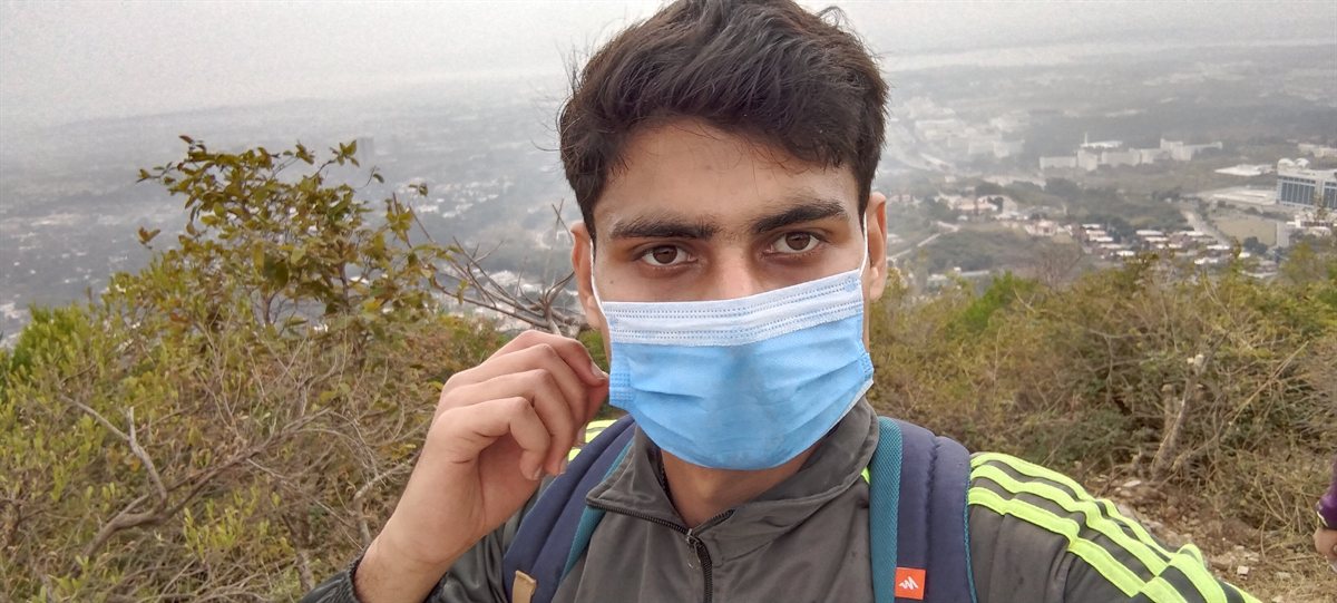 Zubair Zafar at the top of a hill trail, with a hazy city and valley spread out below