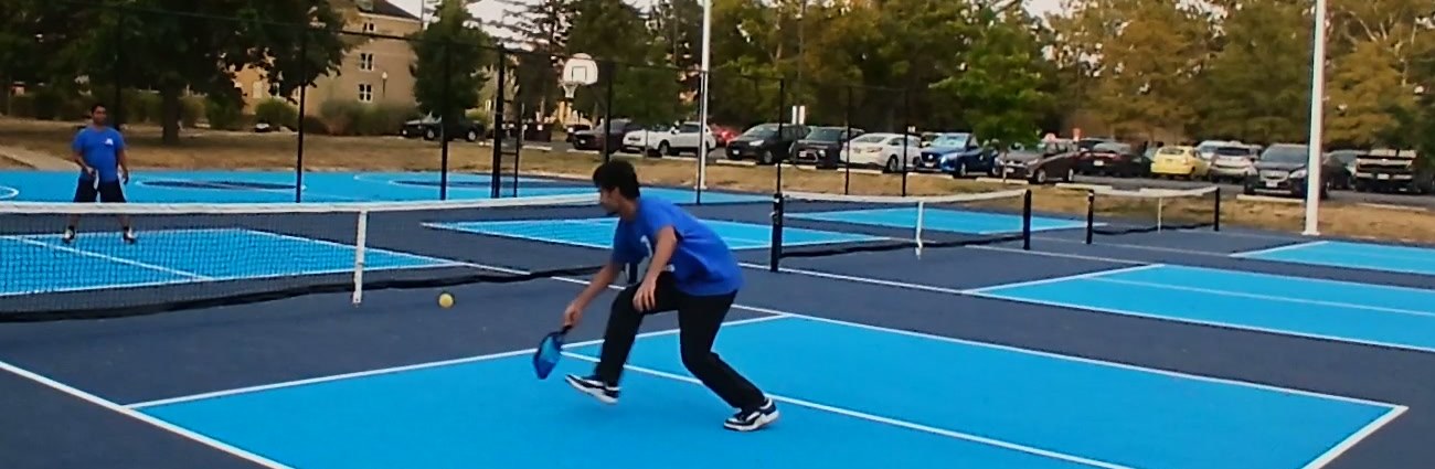 Zubair Zafar dropping low with the paddle back as the ball comes over the net on an outdoor pickleball court