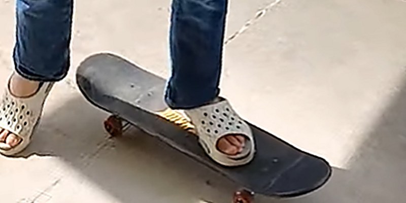 Both feet balanced on a skateboard on a backyard patio, one on the deck and one on the ground